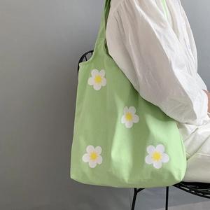 Detail of light green floral canvas tote bag with white daisy patterns worn on shoulder