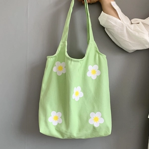 Detail of light green floral canvas tote bag with white daisy patterns and shoulder straps