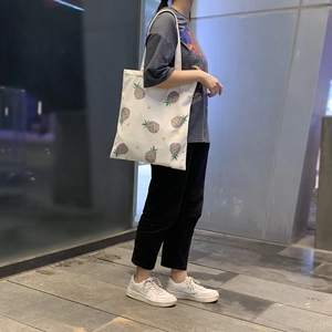 Détail d'un sac cabas en toile blanche à motif d'ananas porté par un mannequin en ville