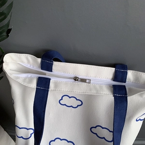 Détail du sac cabas en toile blanche avec imprimé nuages bleus et fermeture zippée robuste