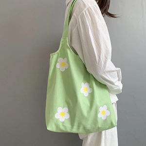 Close-up of green canvas tote bag with daisy pattern worn by a model against a grey wall