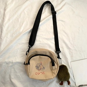Détail d'un sac bandoulière en toile beige avec illustration mouton et pendentif peluche
