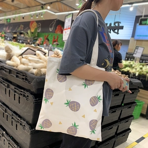 Détail du sac cabas en toile blanche avec motif ananas violet porté par un mannequin
