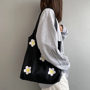 Detail of a black canvas tote bag featuring small white flower prints on the side view
