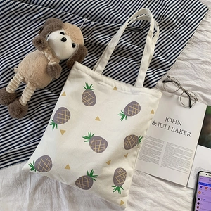 Gros plan d'un sac cabas en toile crème avec imprimé ananas jaune sur le lit