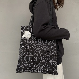 Detail of black canvas tote bag featuring quirky white cartoon emoji prints and plush charm