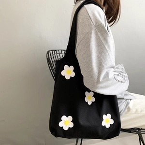 Detail of black canvas tote bag with white daisy prints shown on model's shoulder