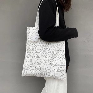 Close-up of a white canvas tote bag with hand-drawn smiley faces and a plush lamb pendant