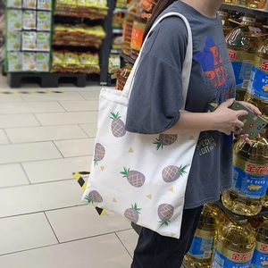 Sac fourre-tout en toile blanche à motif ananas violet présenté dans une scène de shopping