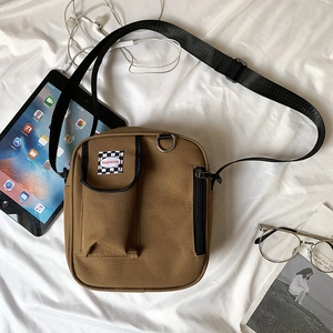 Brown canvas crossbody bag shown with iPad and daily essentials on a white fabric surface