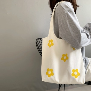 Detailed close-up of a white canvas tote bag with yellow floral prints on a female model