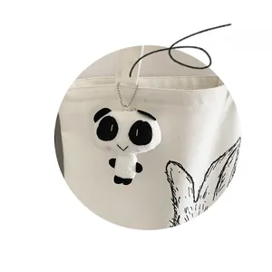Close-up of a cute panda plush keychain accessory on a white canvas shoulder bag