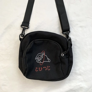 Vue à plat du sac bandoulière en toile noire avec illustration de petit agneau blanc