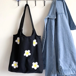 Detail of black canvas tote bag featuring white daisy print hung next to denim jacket
