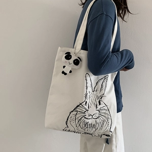 Detailed shot of white canvas tote bag with bunny graphic and plush panda charm detail
