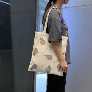 Détail d'un sac cabas en toile blanche avec motifs ananas violets et anses solides