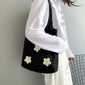 Minimalist black canvas tote bag with white daisy print shown on female model's shoulder