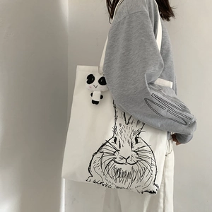 Close-up of white canvas tote bag with rabbit print and cute panda plush pendant accessory