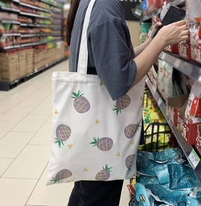Sac fourre-tout en toile blanche avec imprimé ananas violet porté dans un magasin