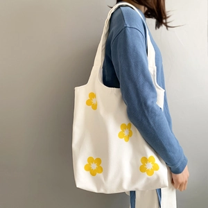 Close-up of white canvas tote bag featuring vibrant yellow flower prints on model shoulder