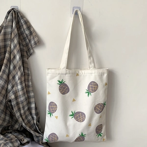 Détail d'un sac cabas en toile blanche avec imprimé ananas violet et anses solides