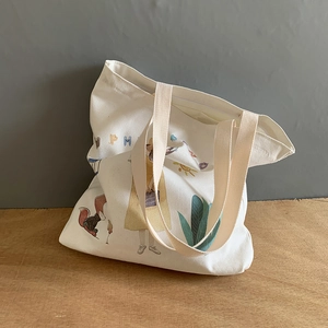 White canvas tote bag with cute Japanese illustration and colorful lettering on grey wall