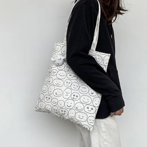 Detail of white canvas tote bag with black smiley print and plush sheep charm on model
