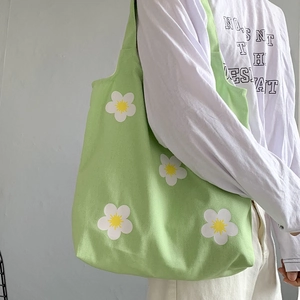 Detail of light green floral canvas tote bag with white daisy patterns worn on shoulder