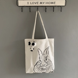 Close-up of a white canvas tote bag featuring a cute rabbit print and a panda plush charm