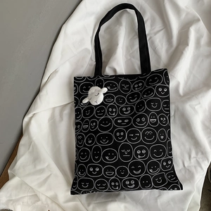 Detail of black canvas tote bag with white smiley faces and a white plush sheep charm