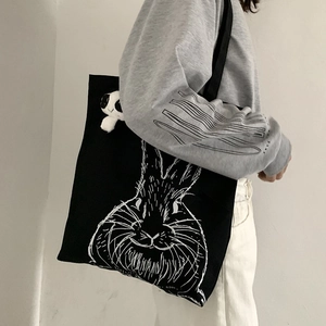Detail of black canvas tote bag featuring white rabbit print and plush panda pendant