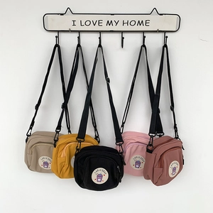 Detalle de varios bolsos bandolera de lona de colores colgados en ganchos decorativos