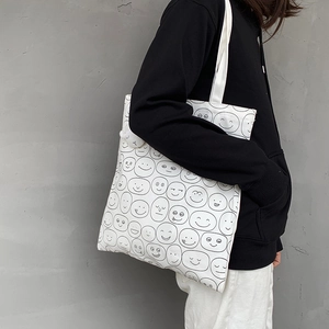 Detail of white canvas tote bag with black cartoon smiley patterns worn by a model