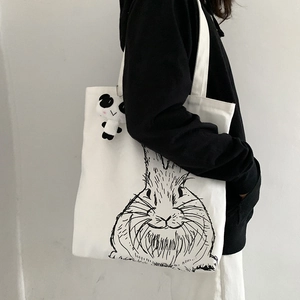 Detail of white canvas tote bag with rabbit print and cute mini panda plush charm