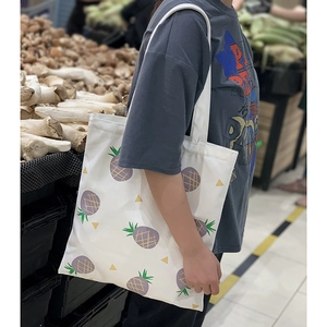 Vue détaillée du sac en toile blanc avec imprimés ananas violets dans un marché local