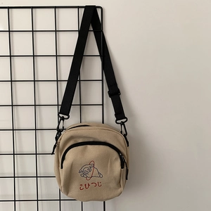 Détail du sac à bandoulière en toile beige avec broderie d'agneau et sangle réglable
