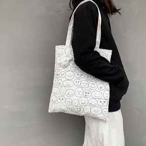 Detail of white canvas tote bag with black smiley print and white alpaca plush charm