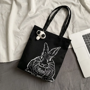 Detail of black canvas tote bag with rabbit print and cute panda plush pendant