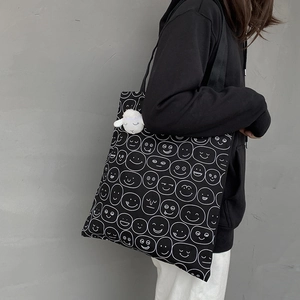 Detail of black canvas tote bag with white smiley faces and plush lamb keychain accessory
