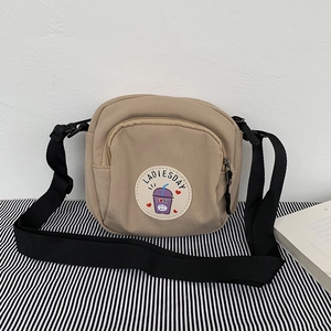 Detalle del bolso bandolera de lona caqui con parche y correa negra ajustable