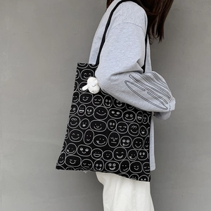 Detail of black canvas tote with white smiley patterns and a plush lamb pendant