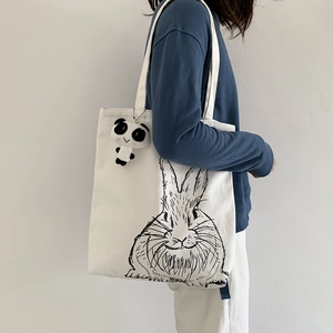 Detail of white canvas tote bag with cute rabbit print and panda plush pendant accessory