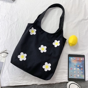 Macro detail of black canvas tote bag featuring white daisy prints and wide shoulder strap