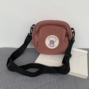 Detalle de bolso bandolera de lona rosa con parche de dibujos y correa de tela negra