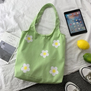 Flat lay of green floral canvas tote bag with daisy print and lifestyle accessories