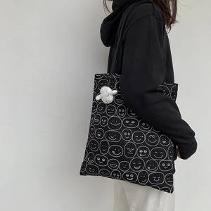 Close-up of black canvas tote with cartoon prints and a cute plush lamb pendant