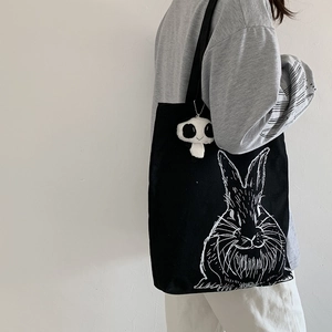 Detail of black canvas tote bag featuring white rabbit illustration and mushroom pendant