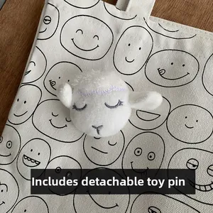 Close-up of detachable white plush lamb pin with purple embroidery on canvas tote bag
