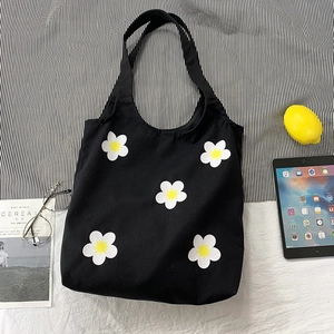 Flat lay of a black canvas tote bag featuring daisy flower prints with aesthetic accessories