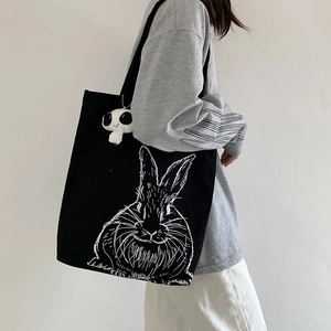 Close-up of black canvas tote bag with hand-drawn rabbit print and panda plush charm